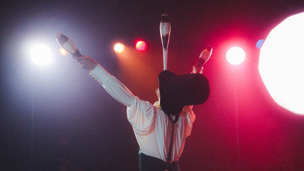 A circus performer juggles three bowling pins, showcasing their skill