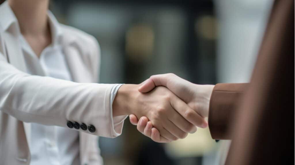 A woman in business attire shakes hands with a man. The image is cropped to cut off their faces.