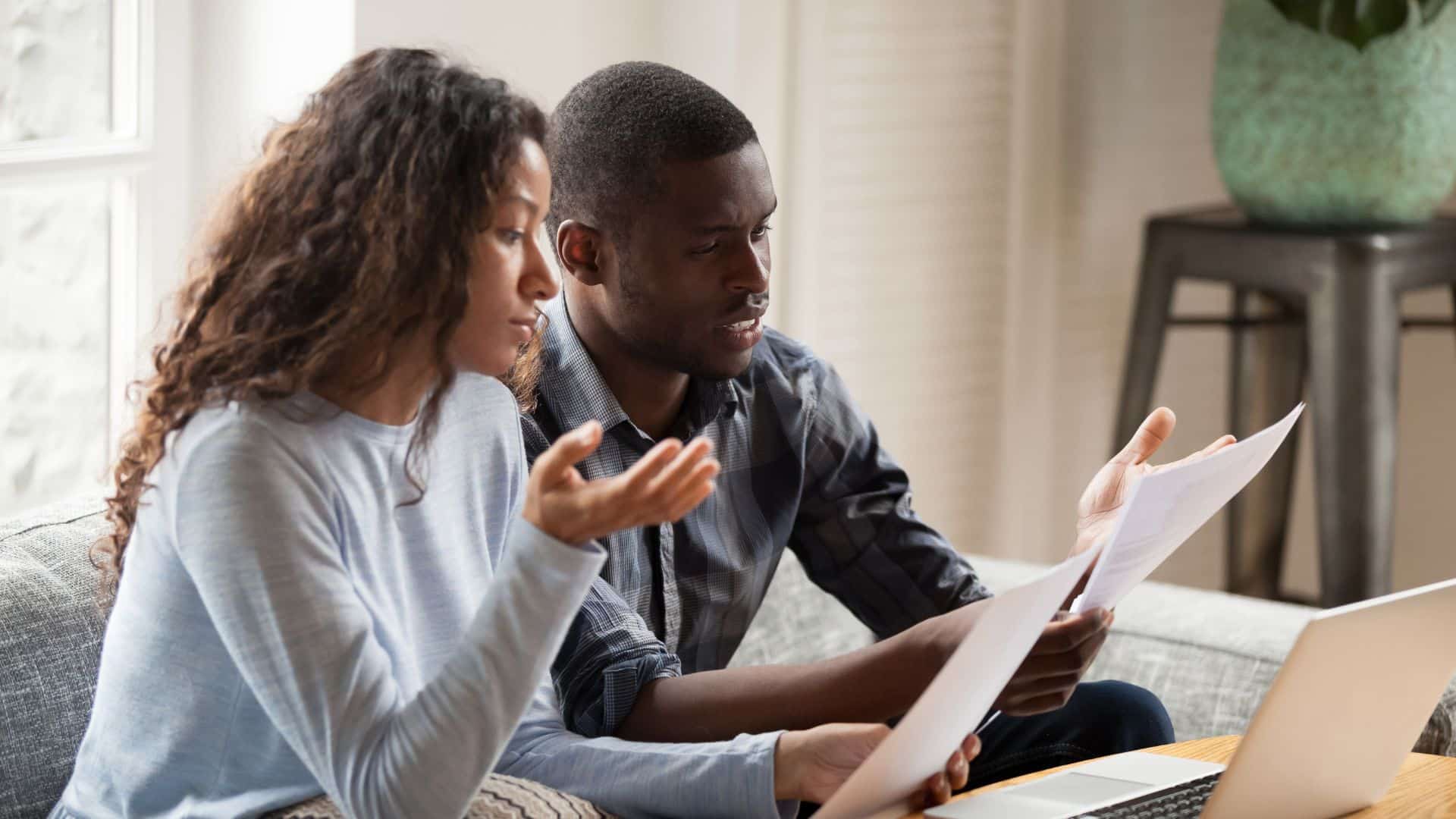 Business owners sitting on couch with laptop on coffee table trying to understand paperwork for BOI reporting guidelines
