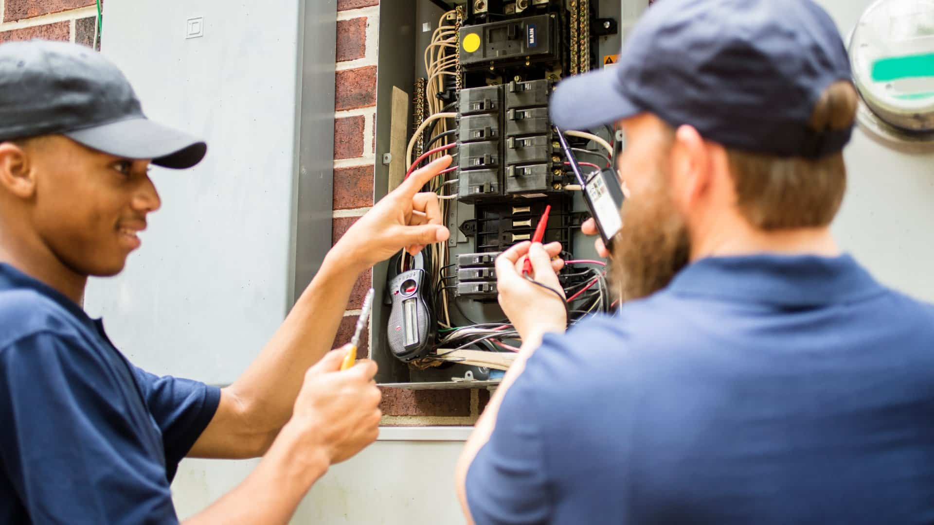 Two electricians work on a fuse box.