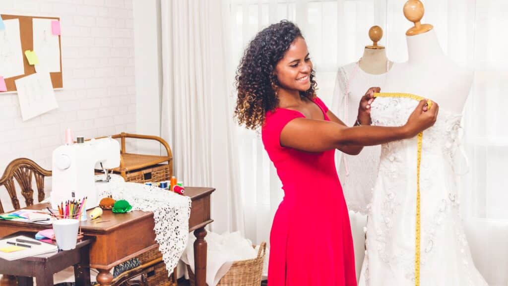 Tailor smiling while taking measurements of a wedding dress.